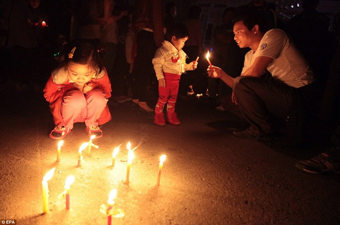 Một em bé đang ngắm nghía những ngọn nến tỏa sáng lung linh trên nền đất trong Giờ Trái đất tại Hà Nội, Việt Nam.