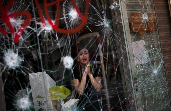 Mirian Burrueco, 30 tuổi, cầu nguyện trong sợ hãi bên trong nhà hàng khi chứng kiến ô cửa kính đầy vết nứt do bị ném đá bởi những người biểu tình tại Barcelona, Tây Ban Nha ngày 29/3. Hàng ngàn công nhân trên khắp đất nước Tây Ban Nha tham gia đình công yêu cầu cải cách lao động đã đụng độ với cảnh sát.