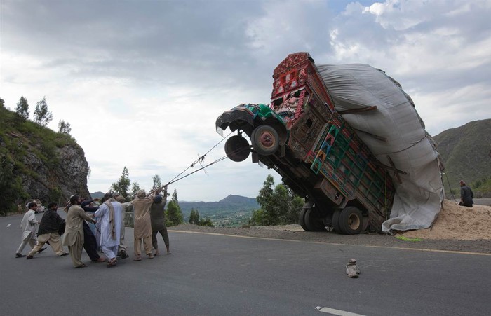Những người đàn ông dùng dây thừng trong nỗ lực đưa chiếc xe chở quá tải bị lật về phía sau trở lại vị trí cân bằng trên một con đường ở Dargai, huyện Malakand, cách khoảng 100 dặm về phía tây bắc thủ đô Islamabad của Pakistan ngày 13/4.