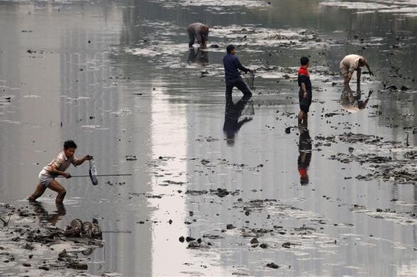 Người câu cá lội qua bùn lầy để bắt cá tại một con kênh ô nhiễm nằm trong trung tâm thành phố Bắc Kinh, Trung Quốc ngày 21/10/2010.