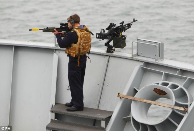 Một thủy thủ cầm súng đứng trên mạn tàu HMS Bulwark