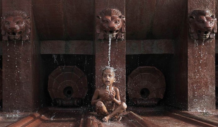 Một cậu bé ngồi dưới đài phun nước trong một ngày nóng nực ở New Delhi, Ấn Độ hôm 31/5 khi nhiệt độ lên tới 39,5 độ.