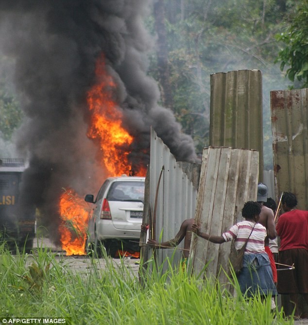 Thổ dân Papua dùng những tấm tôn làm lá chắn đang di chuyển tới gần một xe cảnh sát bị đốt cháy tại làng Kwamki Lama , huyện Mimika.