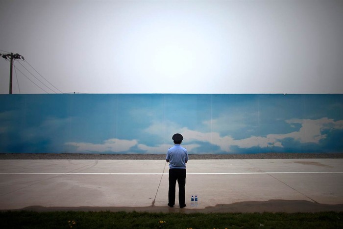 Một nhân viên bảo vệ đứng trước bức tường sơn hình bầu trời trong xanh tại Bắc Kinh, Trung Quốc ngày 18/6.
