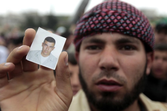 Một người biểu tình giơ tấm ảnh thân nhân đã thiệt mạng khi mọi người tụ tập xung quanh các quan sát viên Liên Hợp Quốc tại làng Azzara, tỉnh Homs ngày 4 tháng 5 năm 2012.