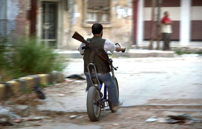 Một phiến quân Syria cưỡi xe đạp đi qua khu phố Khaldiyeh, tỉnh Homs ngày 14 tháng 5 năm 2012.