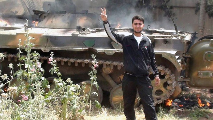 Thành viên lực lượng quân sự Syria tự do chụp ảnh lưu niệm bên chiếc xe tăng đang cháy sau khi đánh bại quân đội chính phủ tại Rasten, Homs ngày 14 tháng 5 năm 2012.