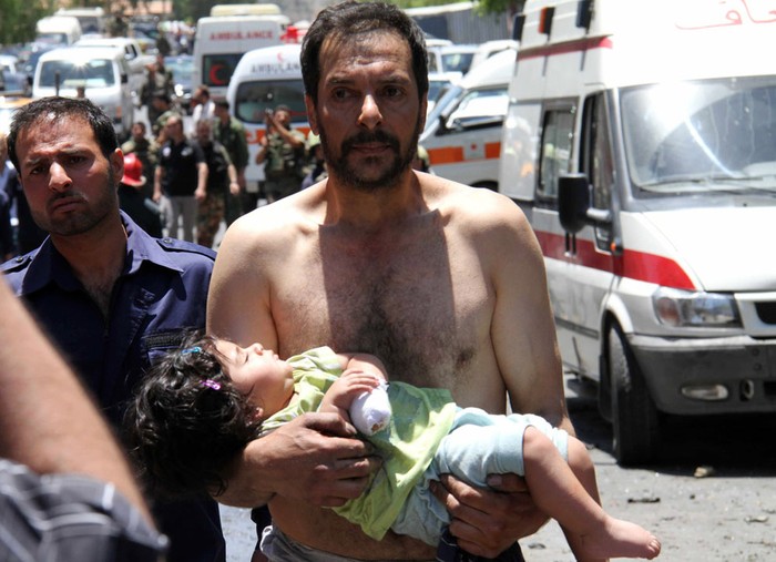 Một người đàn ông bế bé gái bị thương tới chỗ các xe cứu thương sau một vụ nổ nhằm vào một xe buýt quân sự gần Qudssaya, một khu phố của thủ đô Damascus ngày 8/6/2012.