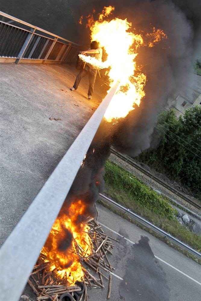 Khoảnh khắc lửa bén lên người một thợ mỏ sau khi anh đổ xăng từ trên cầu xuống đống củi và lốp xe đang cháy ở bên dưới nhằm chặn đường trong một cuộc biểu tình của thợ mỏ vùng Pozo Soton, miền bắc Tây Ban Nha ngày 4/7.