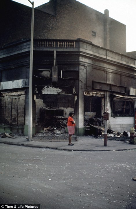 Một phụ nữ gốc Phi đứng bên ngoài những ngôi nhà bị phá hủy và đốt cháy.