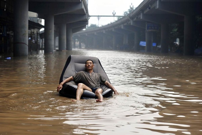 Một người đàn ông ngồi trên chiếc ghế hơi di chuyển trên con phố ngập nước ở Trùng Khánh, Trung Quốc ngày 25 tháng 7.