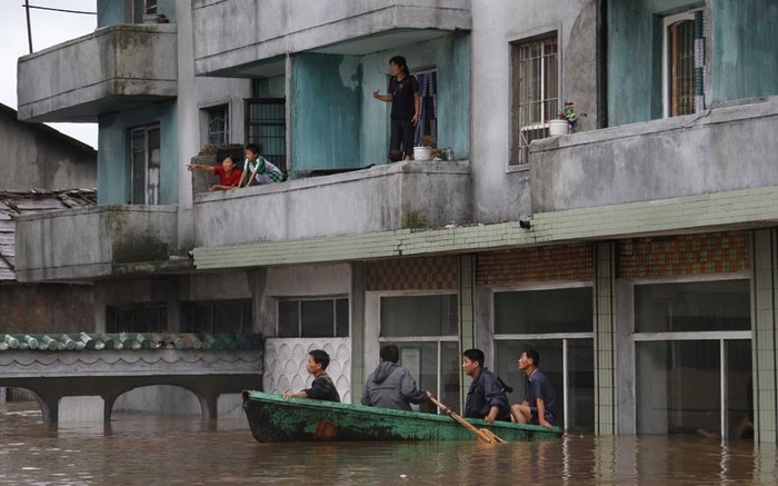 Cư dân chờ đợi trên ban công của một tòa nhà, trong khi những người khác dùng thuyền đi lại trong thành phố Anju bị ngập nước.