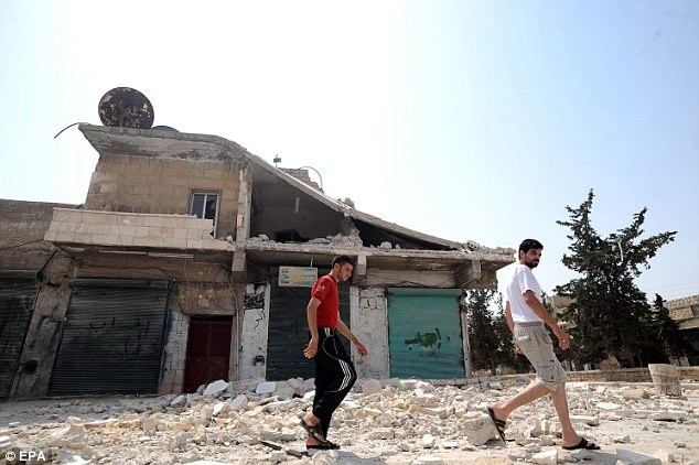 Hai người Syria đi qua một ngôi nhà bị phá hỏng bởi các cuộc giao tranh ở Aleppo.