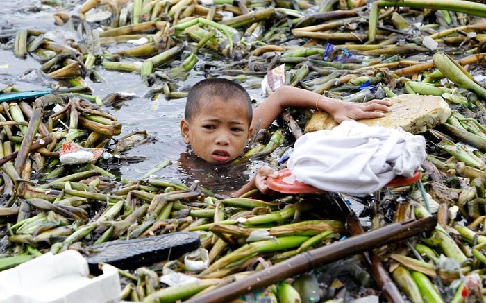 Một cậu bé bỏ chiếc áo sơ mi trên nắp thùng nhựa để giữ cho nó khô trong khi đi thu gom vật liệu tái chế do bão mang tới tại Manila.