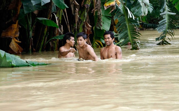 Những người đàn ông di chuyển trong nước ngập tới ngực khi trở về nhà của họ ở quận Quezon, Metro Manila.