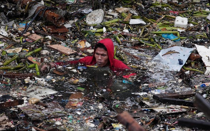 Một người đàn ông đang cố gắng vớt lại những gì còn dùng được sau khi bão làm 2 chiếc xà lan đâm vào khu nhà tồi tàn của anh tại Manila.