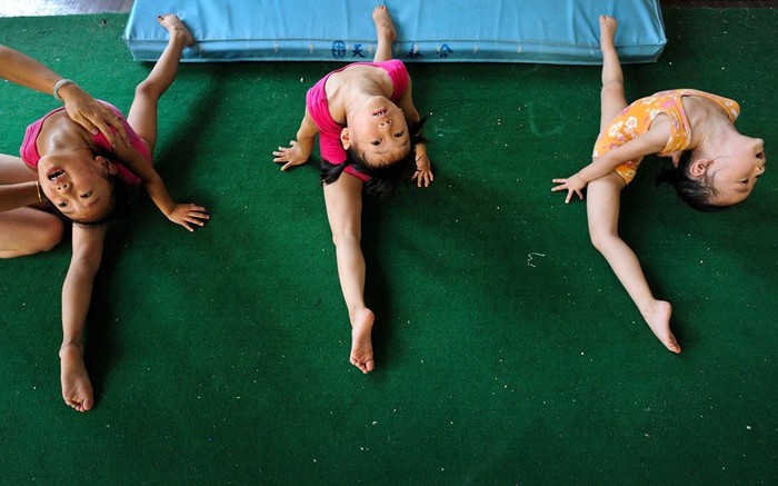 Một huấn luyện viên giúp các bé gái thuộc đội tuyển thể dục dụng cụ thực hiện một bài tập tại trường thể thao ở Nam Kinh.
