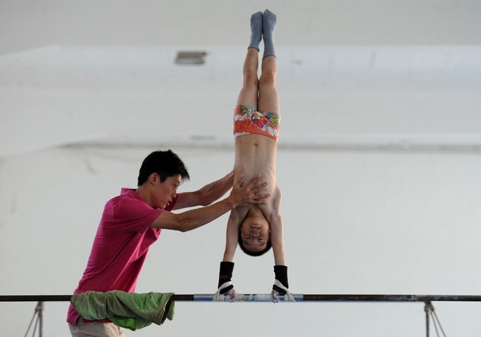 Huấn luyện viên giúp một cậu bé đội thể dục dụng cụ trong quá trình tập luyện tại một trường thể thao ở Nam Kinh