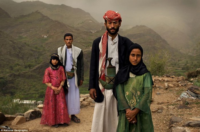 Tahani (áo hồng), người đã kết hôn ở tuổi lên sáu, cùng bạn học cũ Ghada - cũng là một cô dâu trẻ, đứng cạnh chồng của họ trước hiên nhà ở Hajjah, Yemen.