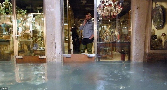 Một chủ cửa hàng cố gắng ngăn nước tràn vào bên trong gian hàng bán đồ lưu niệm của mình.