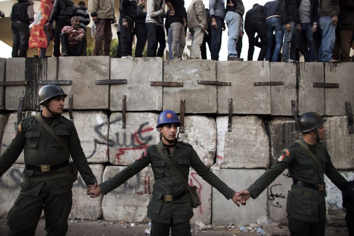 Binh lính Ai Cập đứng chắn phía trước người biểu tình đang đứng trên hàng rào bê tông được quân đội thiếp lập để bảo vệ dinh Tổng thống tại Cairo hôm 11/12.