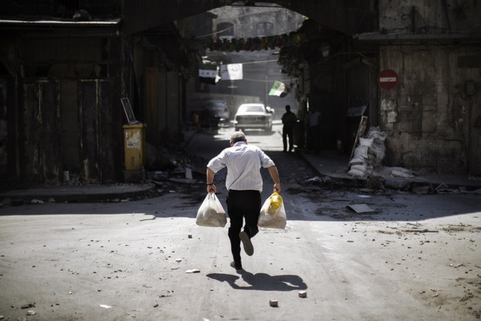 Một người đàn ông Syria mang túi hàng tạp hóa cố gắng né đạn khi chạy qua con hẻm gần trạm kiểm soát của quân nổi dậy tại Aleppo, Syria ngày 14/9.
