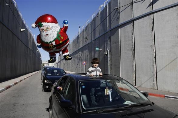 Một cậu bé cầm quả bóng mang hình ông già Noel chuẩn bị qua một trạm kiểm soát của Israel để tới thành phố Bờ Tây Bethlehem ngày 24/12.