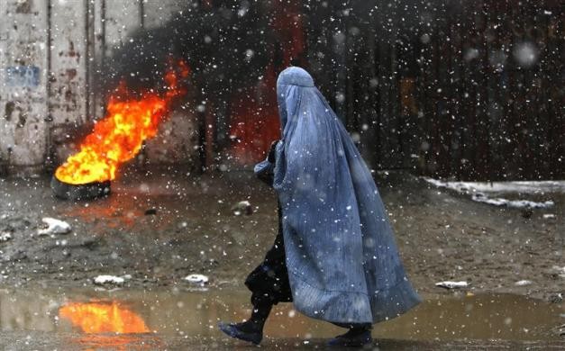 Một phụ nữ Afghanistan đi bộ qua chiếc lốp xe được người dân đốt để sưởi ấm trong ngày tuyết rơi tại Kabul hôm 27/12.