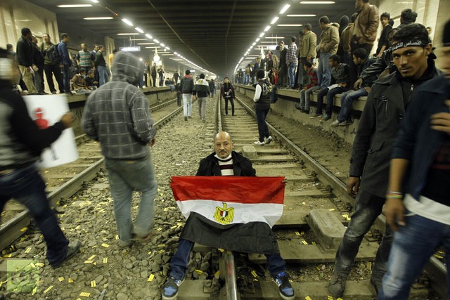 Một người biểu tình Ai Cập giữ quốc kỳ nằm trên đường ray tàu điện ngầm ở Quảng trường Tahrir sau khi người biểu tình đóng cửa nhà ga này vào ngày 25 tháng 1 năm 2013.