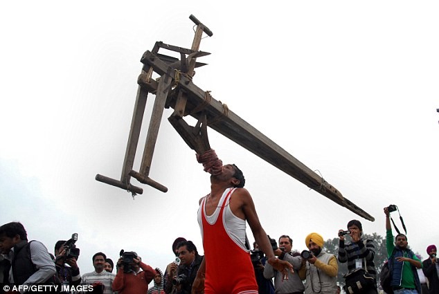 Một nông dân Ấn Độ biểu diễn tiết mục nâng máy cày bằng răng.