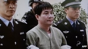 Naw Kham mặc một chiếc áo len màu be và quần xám, hơi mỉm cười khi được dẫn tới phòng tử hình ở nhà tù Côn Minh, tỉnh Vân Nam - CCTV tường thuật.