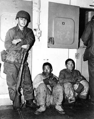 Lính Mỹ đứng bên cạnh hai tù binh trên đường từ Hungnam tới Pusan trong tháng 12/1950.