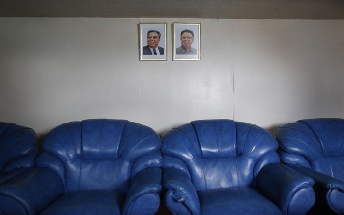 Một căn phòng được trang trí ảnh chân dung hai nhà lãnh đạo quá cố của Triều Tiên, Kim Nhật Thành và Kim Jong-il phía trên những chiếc ghế sô pha màu xanh.