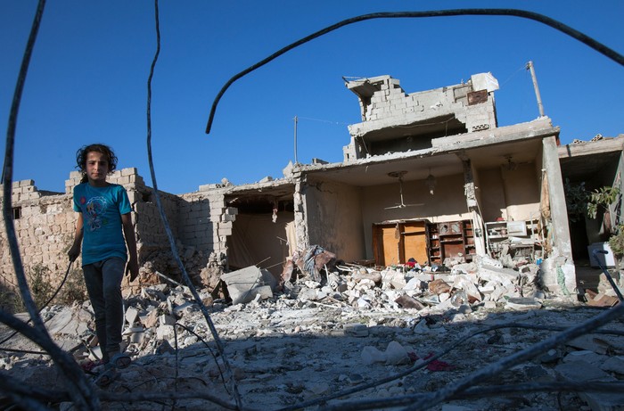 Một cô gái đi bên cạnh đống đổ nát của ngôi nhà của mình sau khi nó trúng tên lửa tại tỉnh Tây Bắc Idlib của Syria vào ngày 18/7.