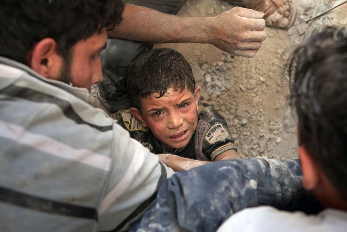 Các tình nguyện viên Syria cố gắng sơ tán Mahmud Fayad (8 tuổi) bị mắc kẹt dưới đống đổ nát của một ngôi nhà bị phá hủy sau khi trúng bom của Không quân Syria ở Saraqeb, tây bắc Syria ngày 20/7.