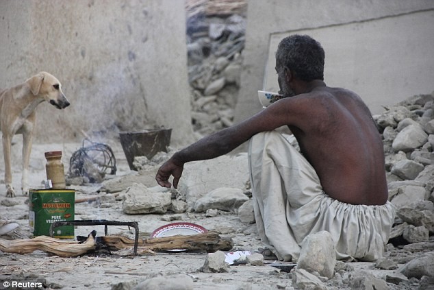 Một nạn nhân sống sót sau động đất ngồi uống trà cạnh đống đổ nát trên nền căn nhà cũ của ông.