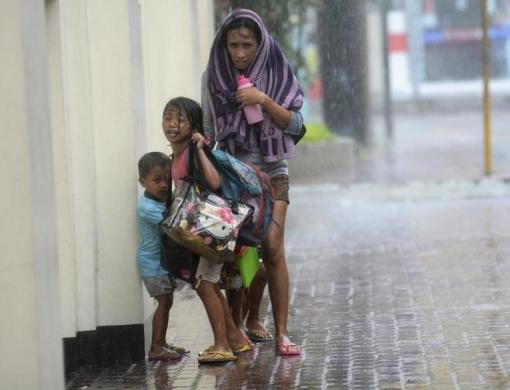 Một phụ nữ và hai đứa con co ro trong mưa gió bão tại thành phố Cebu, miền trung Philippines.