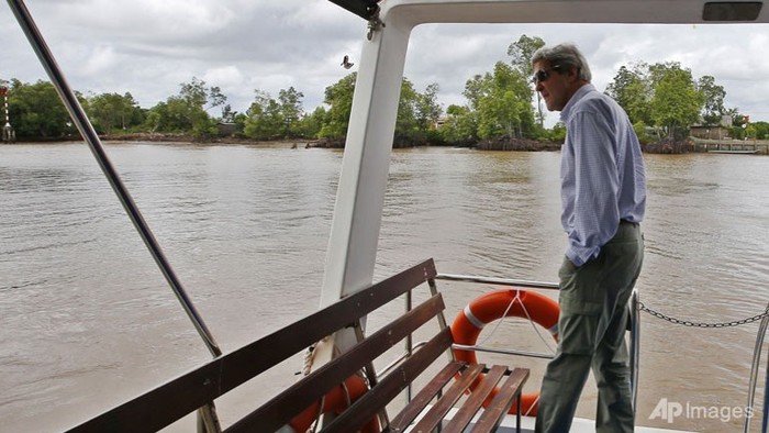 Ngoại trưởng Mỹ đứng trên thuyền quan sát cảnh vật hai bờ sông.