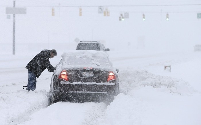 Một người đàn ông đang cố đẩy chiếc xe hơi bị sa lầy trong tuyết tại Zionsvill, bang Indiana.