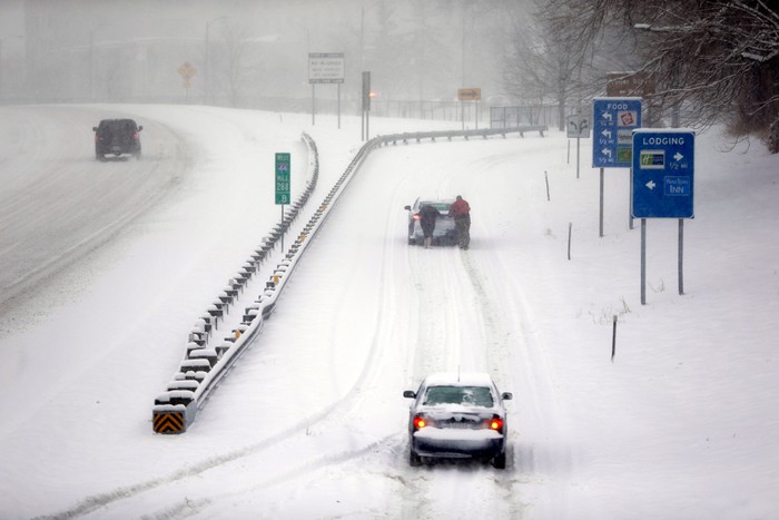 Một cặp đôi đẩy chiếc xe hơi bị kẹt trong tuyết.