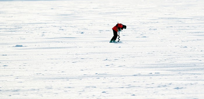 Một người đàn ông dùng khoan điện đục lỗ trên dòng sông băng câu cá ở Minneapolis.