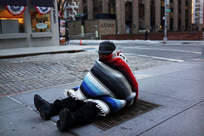 Một người vô gia cư sưởi ấm trên lỗ thông hơi của hệ thống tàu điện ngầm ở New York.