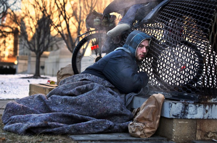 Một người vô gia cư cố nhờ chút hơi ấm từ chiếc xe để sưởi.