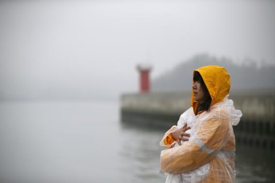 Một phụ nữ mặc kệ mưa gió và lạnh giá nhìn chằm chằm ra phía biển chờ đợi tin tức.