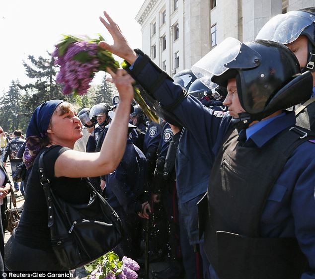 Người biểu tình ném hoa vào một cảnh sát bảo vệ tòa nhà công đoàn bị đốt cháy khi đi tưởng niệm các nạn nhân.