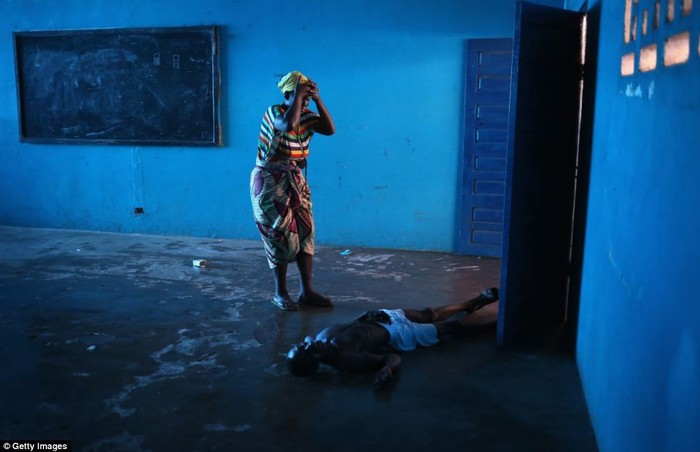 Người phụ nữ ôm đầu khóc khi thấy chồng nghi nhiễm Ebola nằm bất tỉnh trên đất.