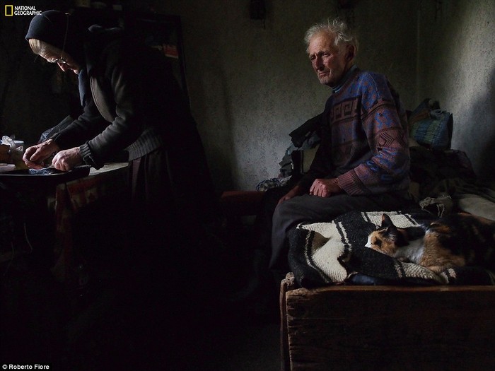 Người đàn ông lớn tuổi đang đăm chiêu khi vợ chuẩn bị bánh để được ban phước trong Bí Tích Thánh Thể tại làng Sarbi, Romania.