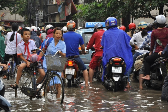 Nước ngập cao nên đi xe đạp khó khăn, một phụ huynh phải xuống dắt xe trong khi con vẫn ngồi ở trên cho khỏi ướt