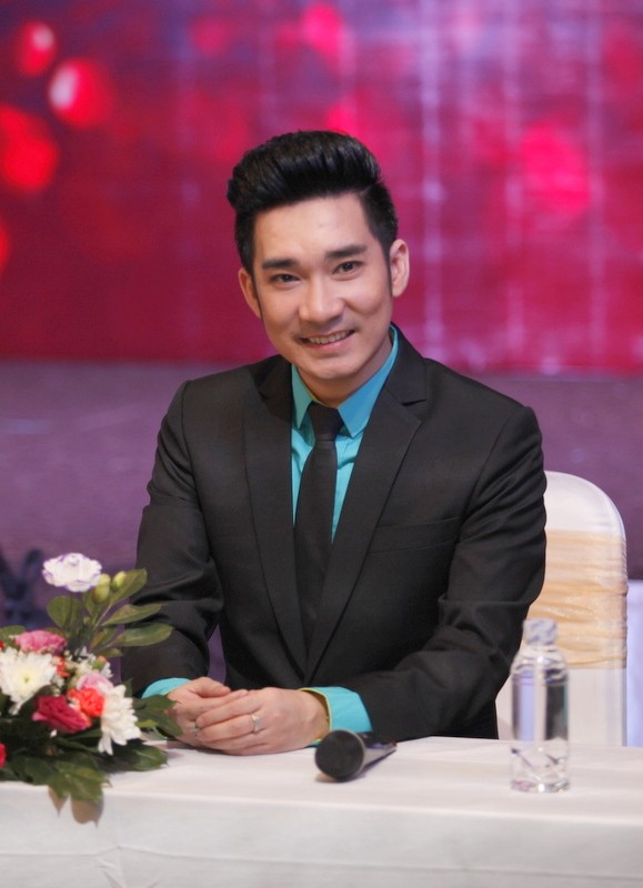 Ca sĩ Quang Hà lịch lãm trong bộ vest đen, áo sơ mi xanh nổi bật tại buổi họp báo.