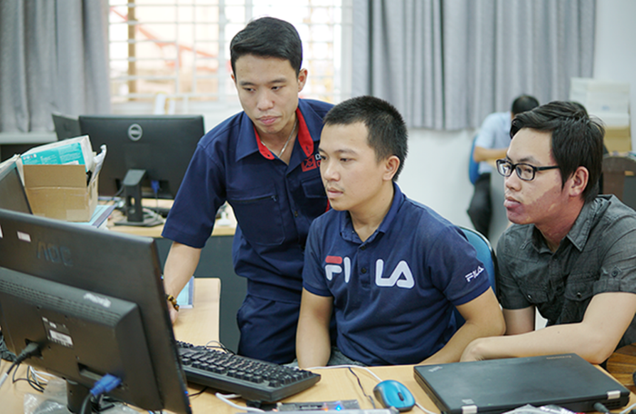 Nhóm sinh viên Nguyễn Thế Đức và Hồ Văn Chương đang được kỹ sư Tạ Quốc Việt (người đứng) hướng dẫn hoàn thiện sản phẩm. Ảnh: AN